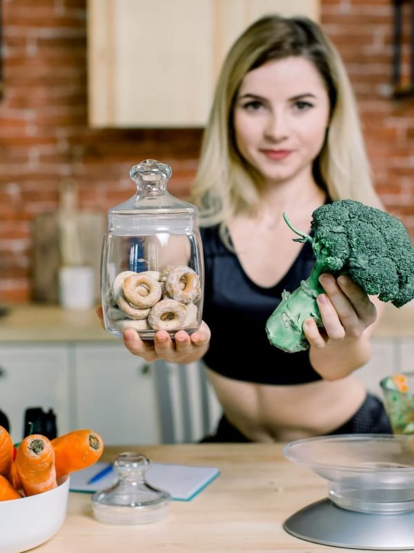 young-woman-in-black-sport-clothes-choosing-between-broccoli-or-junk-food-bagels-healthy-clean-1.jpg